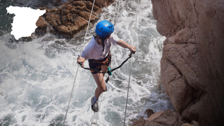 Zdjęcie z Via Ferraty Cala Moli - uczestniczka stoi na linie nad falami