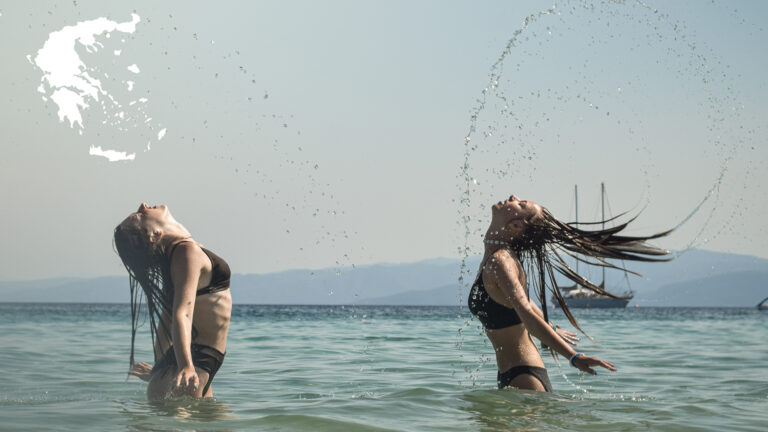 Dwie uczestniczki obozu młodzieżowego Era Wyzwań w Grecji bawią się w morzu, energicznie odrzucając mokre włosy do tyłu