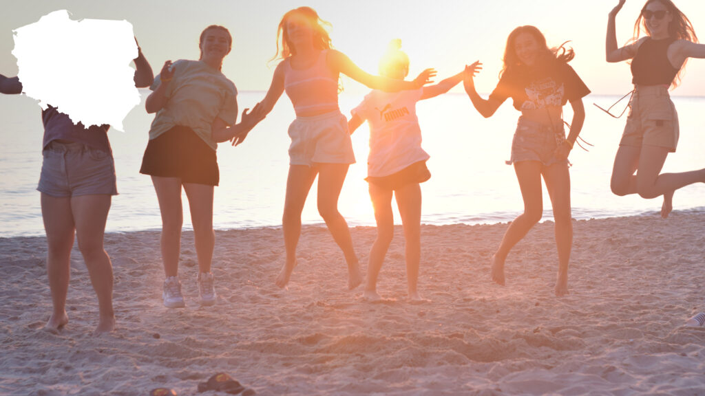 Uśmiechnięte uczestniczki obozu młodzieżowego nad morzem, które skaczą razem podczas zachodu słońca na plaży